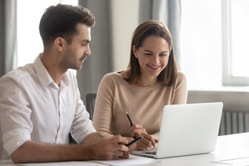 Obraz premium Smiling diverse colleagues work together using laptop