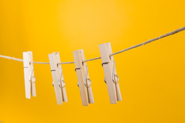 Wooden clothespins hanging on a rope over yellow background.