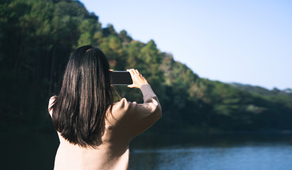 She relax at lake in the forest up on mountain use smartphone for social network.