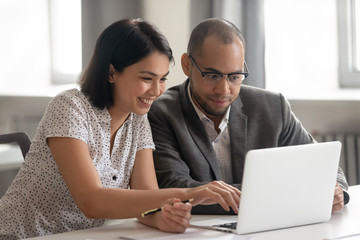 Smiling multiethnic colleagues working together at laptop in office