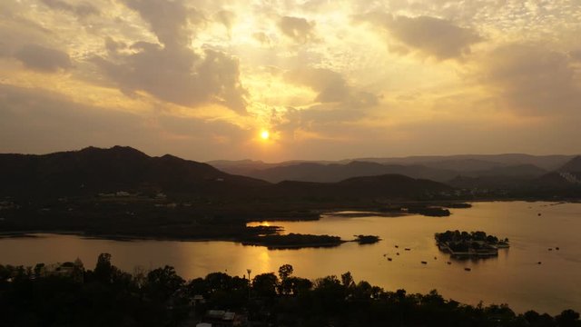 Sunset timelapse video over mountains and lake pichola in Udaipur (Rajasthan), India. Boats in front of island in the middle of the lake.