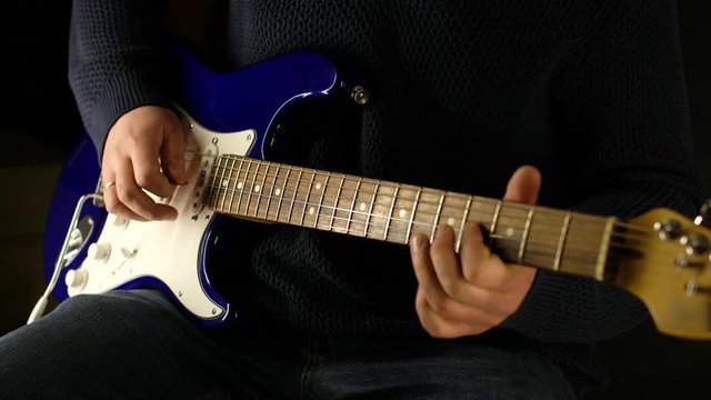 man playing a classic, electric guitar. Black background. the color of the guitar is blue. overall plan. close-up Playing a slow rhythm, busting