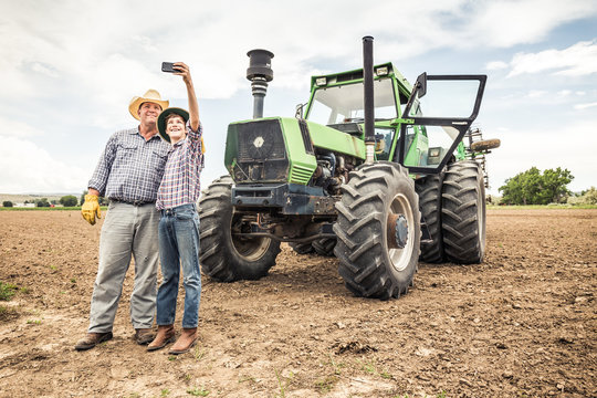 Farmer with son in plowed field with tractor, taking a selfie. Bridger, Montana, USA