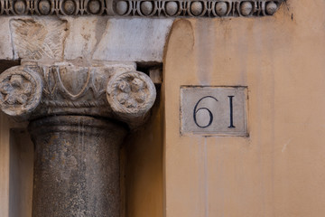 number 61, ancient house number plate on brick wall, Italy