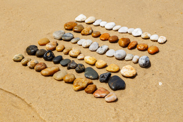 Diagonal in Reihen angeordnete, bunte Steine am Strand, Land Art