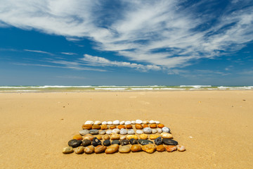 In Reihen angeordnete, bunte Steine am Strand vor blauem Himmel mit Wolken