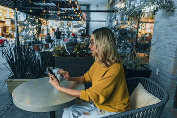 Mujer tomando café en starbucks con celular en mano samsung - obrazy, fototapety, plakaty