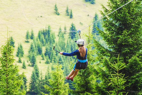 A young girl takes a picture of herself on a cellphone while descending on a zipline_