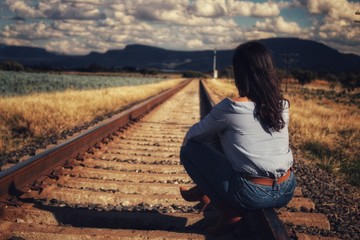 mujer sentada en vias del tren en atardecer