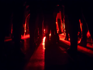 Silhouettes of feet in a nightclub against a bright red lantern in the center with shadows...