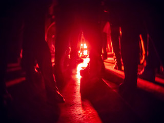 Silhouettes of feet in a nightclub against a bright red lantern in the center with shadows radiating from it on the floor