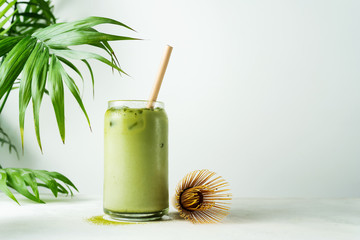 Making Japanese iced matcha latte, green tea with milk, soy milk, traditional matcha tools, with bamboo straw in glass on white background. - obrazy, fototapety, plakaty