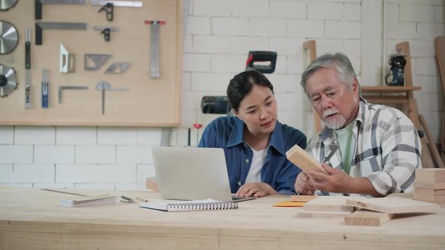 Asian senior male and teenage girl carpenter working design modern furniture in home workshop. Carpenter is high experience and presentation skill in lumber.