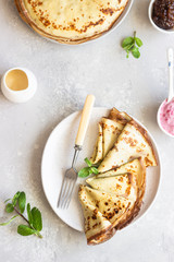 Crepes, thin pancakes with pink yogurt, jam and honey decorated with mint on a ceramic plate. 