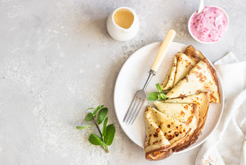 Crepes, thin pancakes with pink yogurt, jam and honey decorated with mint on a ceramic plate. 