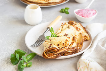 Crepes, thin pancakes with pink yogurt, jam and honey decorated with mint on a ceramic plate. 