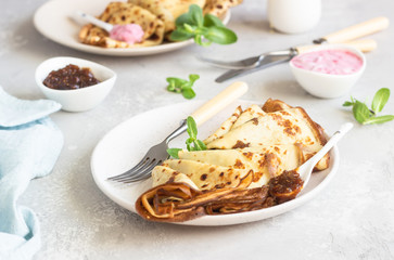 Crepes, thin pancakes with pink yogurt, jam and honey decorated with mint on a ceramic plate. 