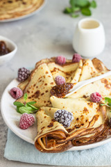 Freshly fried homemade french crepes (thin pancakes) on a ceramic plate with frozen raspberries, blackberries and mint for breakfast or dessert.