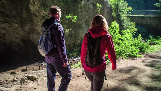 Young couple hiking towards cave exit stop and turn to admire rock formation.