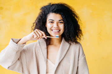 Happy African American woman brushes teeth. Dental hygiene concept. Isolated on pink background.