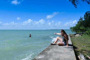 a woman sitting looking out to sea and pointing her finger at the sea