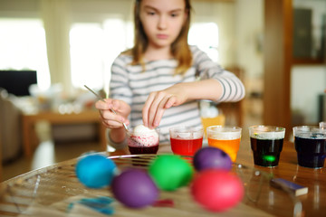 Cute young girl dyeing Easter eggs at home. Child painting colorful eggs for Easter hunt. Kid getting ready for Easter celebration.