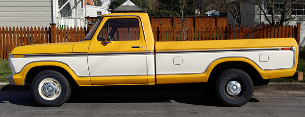 Vintage two tone white and yellow long bed pickup truck parked on neighborhood street.