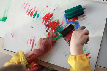 Close up child's hands paint with rollers and sponges and a palette