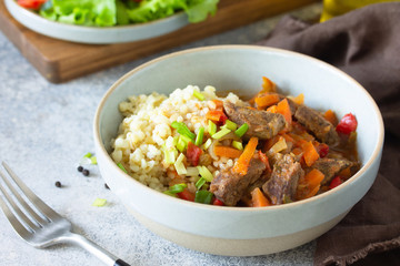 Healthy eating concept. Beef stewed with vegetables in bulgur sauce and fresh vegetable salad on a light stone table top.