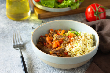 Healthy eating concept. Beef stewed with vegetables in bulgur sauce and fresh vegetable salad on a light stone table top.