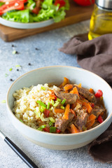Healthy eating concept. Beef stewed with vegetables in bulgur sauce and fresh vegetable salad on a light stone table top. Copy space.