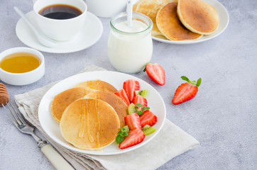 Traditional Russian pancakes on kefir with honey, sour cream, fresh strawberries and kiwi on a white plate with a cup of coffee. Healthy breakfast. Russian maslenitsa. Horizontal orientation.