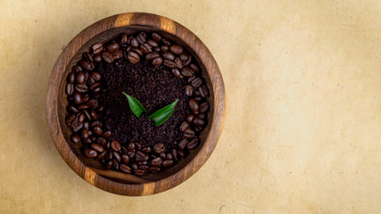 Homemade cosmetics with coffee scrub, beans, and green leaves on wooden bowl on yellow eco friendly background
