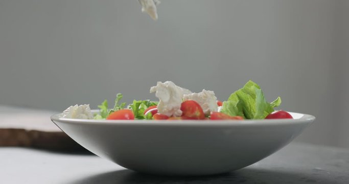 Slow motion add ricotta cheese to cherry tomatoes and frisee leaves into white bowl