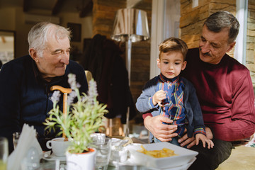 Portrait of senior man 80 years old pensioner sitting in chair with his family son and grandson at the restaurant or home retirement nursery grandfather caucasian child boy