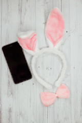 happy Easter. Smartphone layout next to Easter Bunny ears on a light wooden background. Flat lay