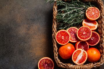 Sliced Sicilian blood oranges with sprigs of rosemary in a wicker basket on a rustic background.