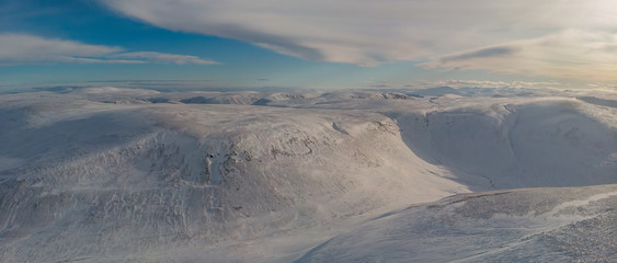 An aerial scenic view of a moutain range in the winter with snowy slope under a majestic blue sky and white clouds