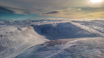 An aerial scenic view of a moutain range in the winter with snowy slope under a majestic blue sky and white clouds