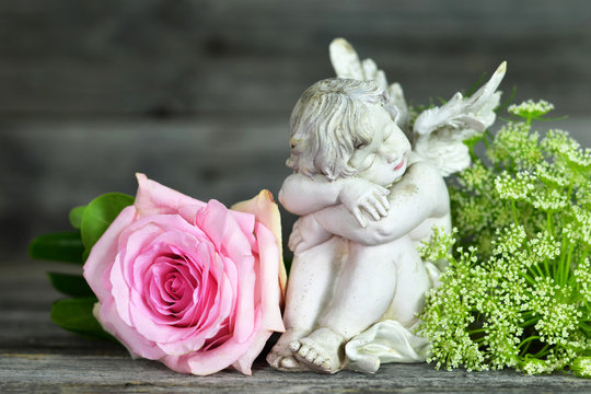 Guardian angel and pink rose on wooden background