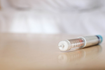 Hypodermic syringes pen with needle lies on table near bed, close up, selective focus