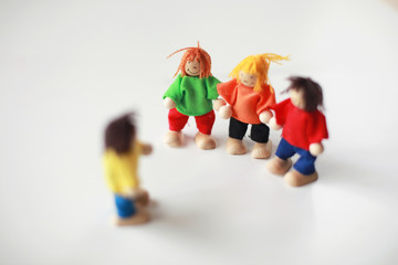 Group of four wooden flexible children puppets in colourful clothes standing on a white table 