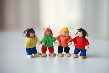 Group of four wooden flexible children puppets in colourful clothes standing on a white table 