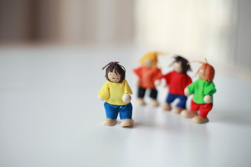 Group of four wooden flexible children puppets in colourful clothes standing on a white table 