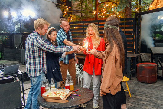 Caucasian Friends Having Garden Party Outside, They Dancing To The Dj's Music With Bengal Lights In House Backyard At Summer Night.