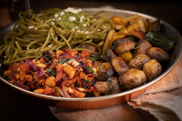 Vegetarian Italian meal consisting of  spinach pasta and pesto, roasted mushrooms and zucchini,  panzanella