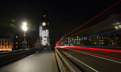 Fototapeta na wymiar city bridge at night, renovated Big Ben clock in background, colorful trails left by left bus