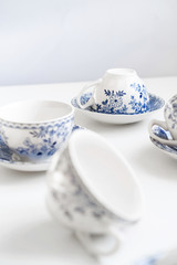 Ceramic saucers with a cup for tea in blue with flowers. New luxury elegance dinnerware on a isolated white background. Trendy plate. Flat lay view.