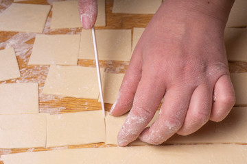 A woman cuts the dough into squares with a white ceramic knife. Plywood cutting board, wooden flour...