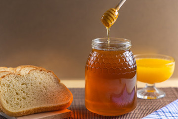Still life with natural honey, orange juice, rustic bread and honey spoon falling on the honey jar